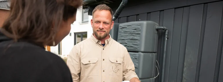 Fachberater erklärt einer Kundin die Regenwassernutzungsanlage am Wohnhaus.
